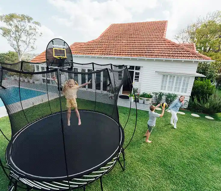Young girl jumping on the trampoline with her brother and mother playing outside