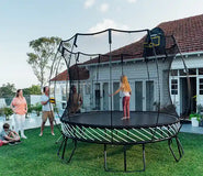 Load image into Gallery viewer, A young girl standing on an outdoor trampoline with her family watching her