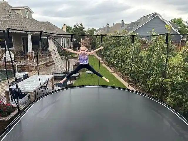 a young girl jumping very high on a trampoline and with arms and legs wide open 