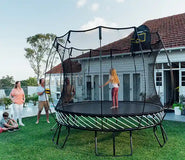 Load image into Gallery viewer, A young girl standing on an outdoor trampoline with her family watching her
