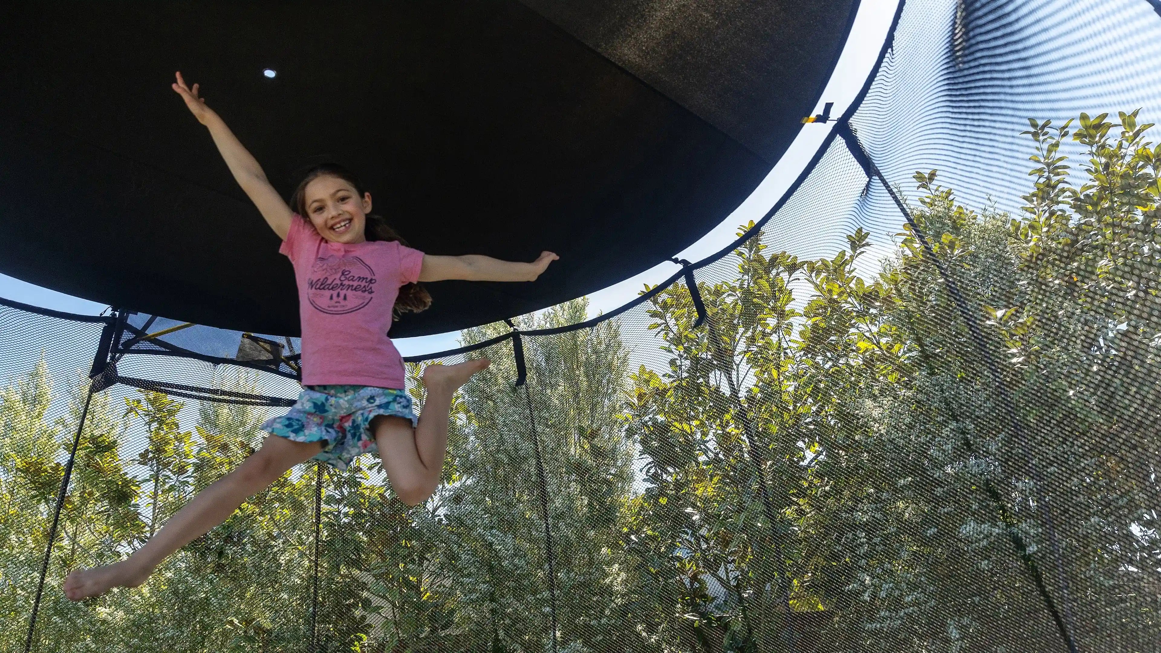 young girl jumping high on a trampoline with sun shade
