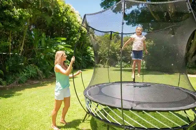 girl jumping on a trampoline with an adult supervising