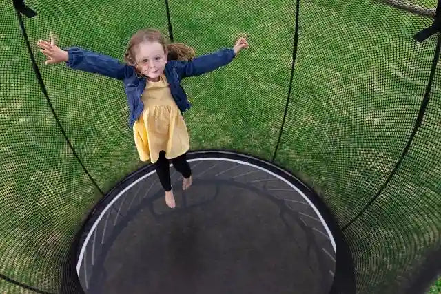 a young girl jumping on an outdoor trampoline